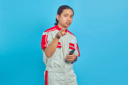 Angry handsome man wearing mechanical uniform using cell phone isolated on blue background