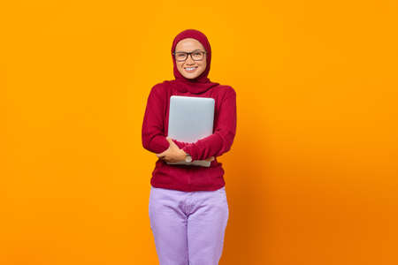 Portrait of smiling Asian woman bring laptop over yellow background