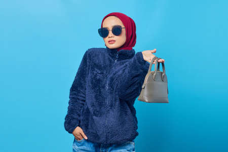 Beautiful young Asian woman holding bag with a happy expression on blue background