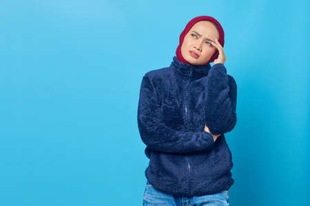 Pensive young Asian woman thinking about something on blue backgroundの写真素材