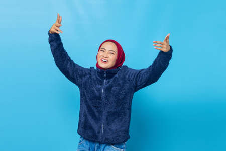 Portrait of beautiful young Asian woman dancing happy and cheerful on blue backgroundの写真素材