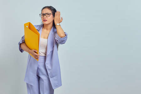 Portrait of serious young Asian business woman keeps hand near ear tries to overhear private...
