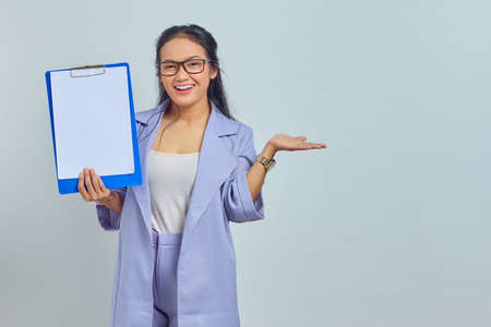 Portrait of cheerful young Asian business woman showing blank clipboard and pointing at copy space...