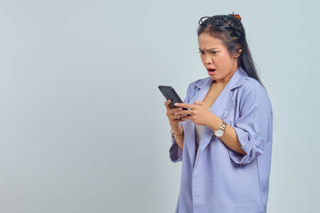 Portrait of surprised young Asian woman using mobile phone isolated on white backgroundの写真素材