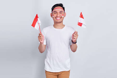 Portrait of Excited young Asian man celebrating indonesian independence day on 17 august and holding indonesian flag isolated on white background studio portraitの写真素材