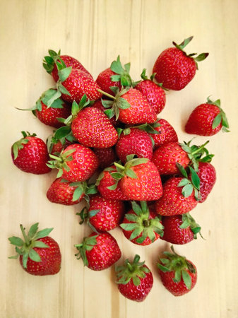 A vibrant pile of fresh organic strawberries on a rustic wooden cutting board, perfect for culinary themes, healthy lifestyle visuals, and seasonal food concepts.の写真素材