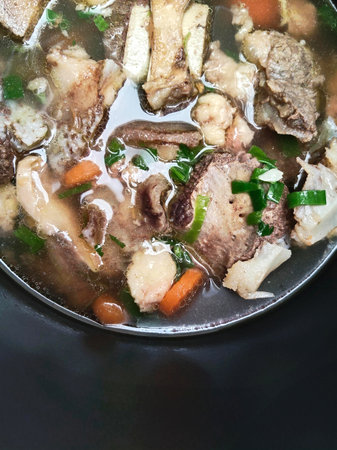 Thai style noodle soup with pork and vegetables in black bowl