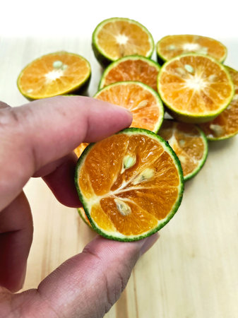 Close up of a hand holding a slice of orange on a wooden board