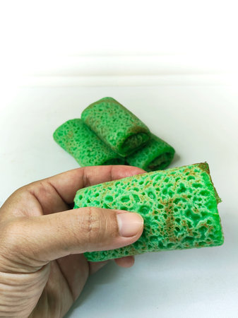 Several pieces of traditional Indonesian Dadar Gulung, a sweet green rolled pancake filled with grated coconut, are neatly wrapped in plastic on a wooden surface.の写真素材