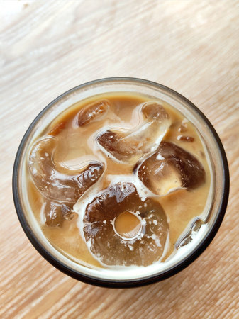 Ice coffee in a glass on wooden table background. Top view.