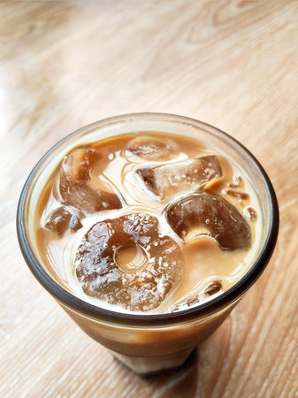 Iced coffee with milk in a glass on wooden table background.