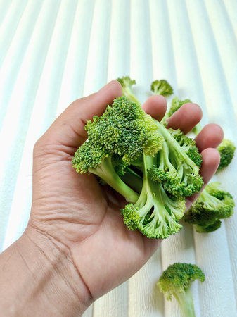 Fresh green broccoli in hand on a white wooden background. Selective focus.の写真素材