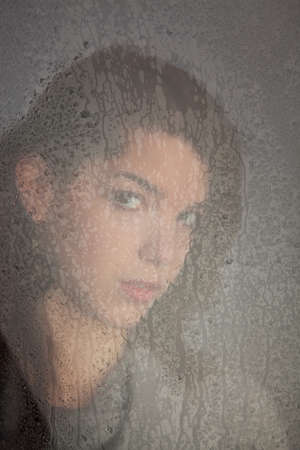 Sad pensive young woman behind a window