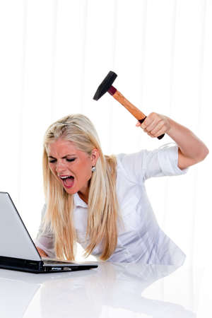 Furious businesswoman with hammer, yelling and preparing to smash her laptop. Vertical.の写真素材