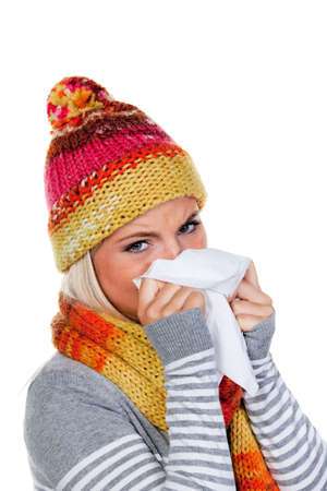 Young woman, wearing a hat and scarf, blows her nose while looking sadly at the camera. Vertical.の写真素材