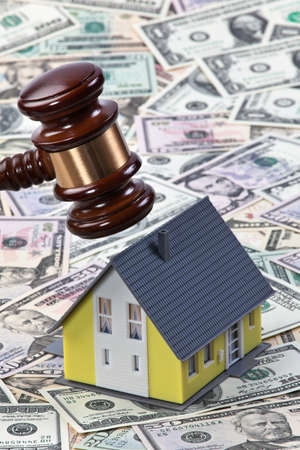 Gavel about to hit a toy house surrounded by cash. Vertically framed shot.の写真素材