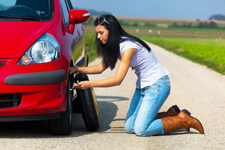 Young woman crouched down and changing a tire on her car. Horizontally framed shot.の写真素材