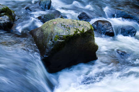 Stream flowing over stones, with large boulder as focus. Horizontally framed shot.の写真素材