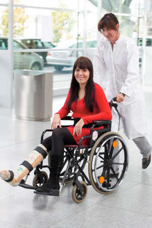 Young woman with a leg cast, wheelchair and nurseの写真素材
