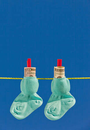 Baby socks on clothesline with dollar bills. Blue sky.の写真素材