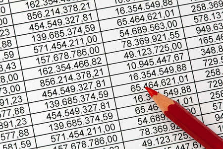 Red pencil on a balance sheet with many numbers. Savings in expenditureの写真素材
