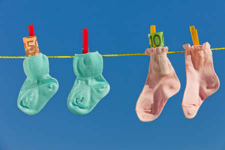 Baby socks on clothesline with ? bills. Blue sky.の写真素材