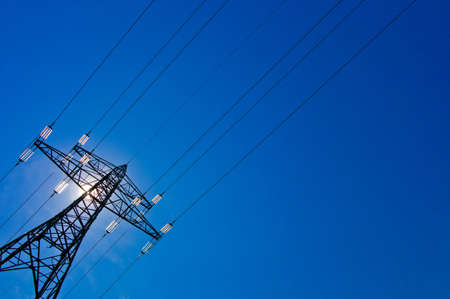 the pylons of a power line with sun and blue skyの写真素材