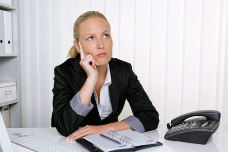 a pensive businesswoman sitting at her desk in an officeの写真素材
