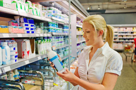 a young woman buys milk at the supermarket  stands in front of the refrigerated section の写真素材