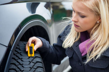 a young woman is measuring the tread depth of her car tire the proper depth in the tread of a tire can prevent accidents a young woman is measuring the tread depth of her car tire the proper depth in the tread of a tire can prevent accidents