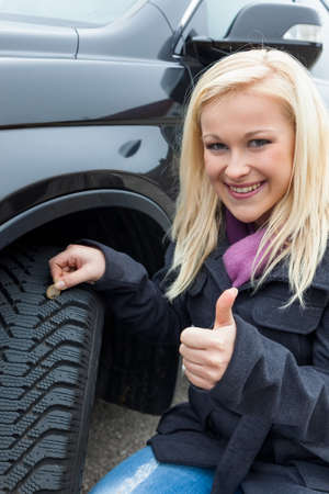 a young woman is measuring the tread depth of her car tire  the proper depth in the tread of a tire can prevent accidents の写真素材
