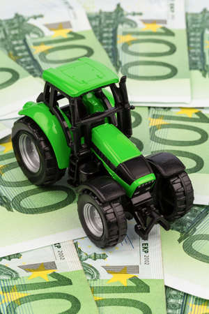 a tractor stands on euro banknotes  symbol photo for costs, revenues and funding of a farmer in agricultureの写真素材