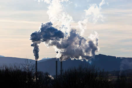 the smoking chimneys of a factory against a blue sky  white smoke rises from chimneys onの写真素材