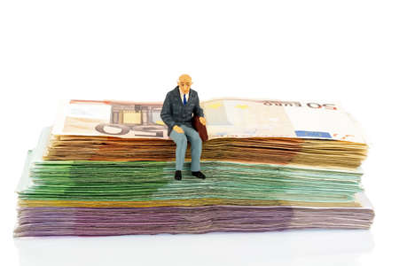 symbolic photo for retirement and old age, figure of an old man sitting on a pile of banknotesの写真素材