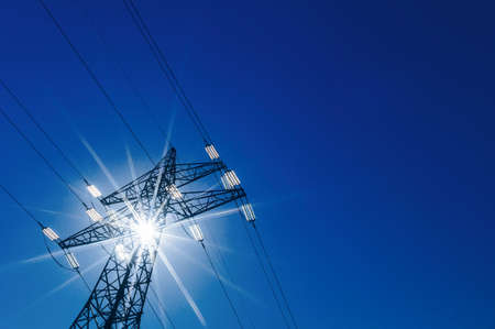a high voltage power pylons against blue sky and sun raysの写真素材