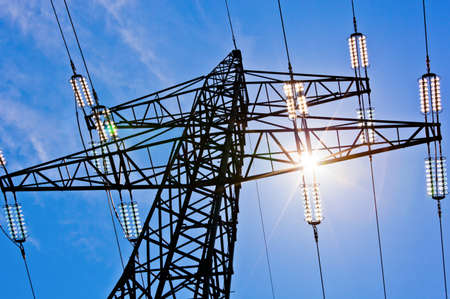 a high voltage power pylons against blue sky and sun raysの写真素材