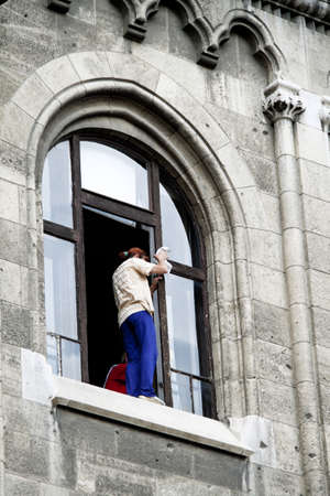 a woman cleans windows and stands dangerously on the window ledge