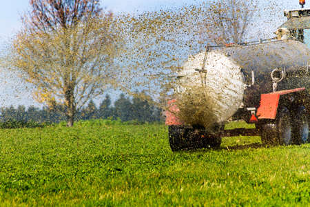 a tractor with manure fertilizes a field in autumnの写真素材