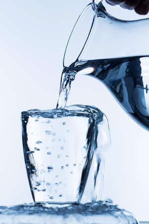 pure water is emptied into a glass of water from a pitcher. fresh drinking water