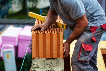 anonymous construction worker on a construction site building a house built a wall of bricks. brick wall of a solid house. icon image for undeclared work and bunglingの写真素材