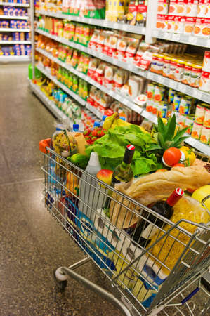 a shopping cart is standing in a aisle of a supermarket between the shelves.の写真素材