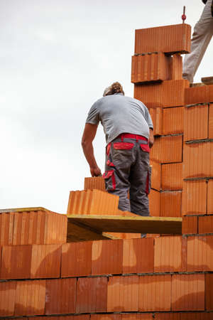 anonymous construction worker on a construction site building a house built a wall of bricks. brick...