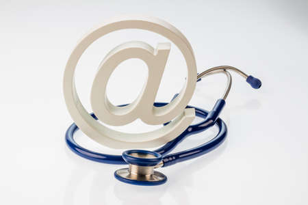 an email sign and a stethoscope on a white background. symbolic photo for internet in the doctor's office.の写真素材