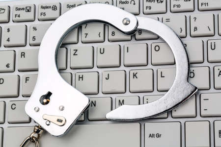handcuffs lying on the keyboard of a computer. symbolic photo for crime, computer crime and misuse of data.の写真素材