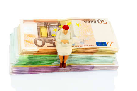 figure of an old woman sitting on a stack of bills, symbolic photo for pension and retirement