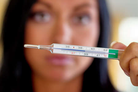 a woman holding a thermometer hindquarters. symbolic photo for sick and fever