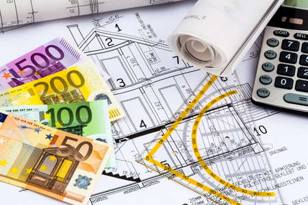 a blueprint of an architect with a calculator and euro money. symbolic photo for funding and planning of a new home.の写真素材