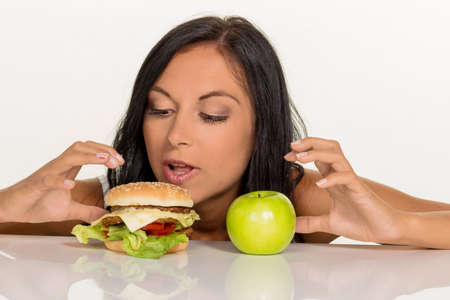 a young woman can not decide between a hamburger and an apple itself. healthy or unhealthy diet.の写真素材