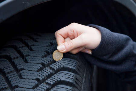 a young woman measures the tread depth of your car tire. the correct depth in the tread of a tire...