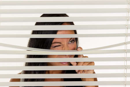 a young woman watching something through the blinds of her windowの写真素材